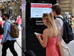 Rail passengers pass an electronic sign in London warning of 'Extremely hot weather' forecast for July 18 and 19, and advising commuters to only travel for essential journeys.