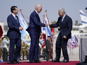 President Joe Biden fists bumps Israeli Prime Minister Yair Lapid, right, after arriving at Ben Gurion Airport, Wednesday, July 13, 2022, in Tel Aviv, as President Isaac Herzog, left, looks on.