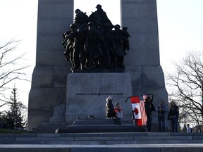 A person holds a combination American and Canadian flag at the Tomb of the Unknown Soldier at the National War Memorial before a march at a demonstration, part of a convoy-style protest participants are calling "Rolling Thunder", in Ottawa, on Friday, April 29, 2022.