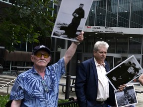 Elder Peter Irniq, holds up a photo of Fr. Johannes Rivoire, who is wanted in Canada for abusing children in Nunavut but now resides in France, as he stands with NDP MPs Charlie Angus outside the Department of Justice during a rally to demand an independent investigation into Canada's crimes against Indigenous Peoples, including those at Indian Residential Schools, in Ottawa on Saturday, July 31, 2021.