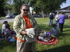 Victoria McIntosh, standing, holds a sweater she wore on her first day of school as supporters perform a ceremony and drum outside court in Powerview, Man., on Wednesday, July 20, 2022. McIntosh alleges 92-year-old priest Arthur Masse assaulted her when she was a student at a former residential school.