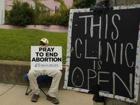 An anti-abortion supporter sits behind a sign that advises the Jackson Women's Health Organization clinic is still open in Jackson, Miss., Wednesday, July 6, 2022. The clinic is the only facility that performs abortions in the state. However, a chancery judge rejected a request by the clinic to temporarily block a state law banning most abortions. Without other developments in the Mississippi lawsuit, the clinic will close at the end of business Wednesday and the state law will take effect Thursday.