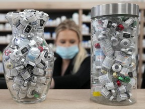 Jars full of empty COVID-19 vaccine vials are shown as a pharmacist works behind the counter at the Junction Chemist pharmacy, in Toronto on Wednesday, April 6, 2022. Albertans over the age of 18 will soon be able to book their fourth dose of the COVID-19 vaccine.