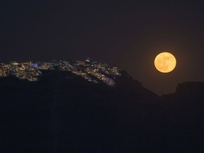 FILE - The strawberry supermoon rises behind the village of Imerovigli on Sandorini's caldera, in Greece's Cyclades islands, on June 14, 2022. If you missed last month's supermoon, you have another chance. This month's full moon is Wednesday, July 13, 2022. At the same time, the moon's orbit will bring it closer to Earth than usual. This cosmic combo is called a supermoon.