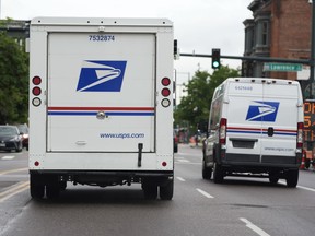 FILE - A USPS logo adorns the back doors of United States Postal Service delivery vehicles as they proceed westbound along 20th Street from Stout Street and the main post office in downtown Denver, Wednesday, June 1, 2022. USPS plans to substantially increase the number of electric-powered vehicles it's buying to replace its fleet of aging delivery trucks, officials said Wednesday, July 20, 2022.