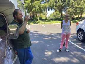 Orson Lee, who's been homeless for six years, drinks water from a water bottle while outreach worker Mary Guiberson looks on at a park in Burien, Wash. The National Weather Service extended its heat advisory by one more day in the Seattle area. Outreach teams have fanned out to provide water and other aid to the homeless.