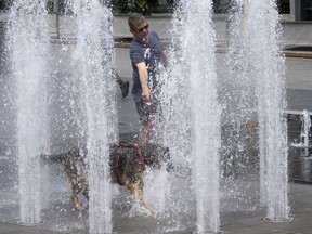 A man cools off his dog at a fountain as temperatures go above 30 C on Wednesday, July 20, 2022 in Montreal. Heat warnings remain in place throughout Eastern Canada, with Environment Canada warning of humidex levels in the mid to high 30s or even 40 C heading into the weekend.