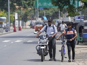 FILE- A motorist pushes his motorcycle along with a cyclist amid fuel shortage in Colombo, Sri Lanka, July 5, 2022. Sri Lanka's central bank has raised its key interest rates to 14.50% and 15.50% to try to contain inflation that has added to the country's economic woes.