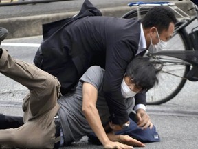 Tetsuya Yamagami, bottom, is detained near the site of gunshots in Nara Prefecture, western Japan, Friday, July 8, 2022. Former Japanese Prime Minister Shinzo Abe, an arch-conservative and one of his nation's most divisive figures, was shot and critically wounded by Yamagami, during a campaign speech Friday in western Japan. He was airlifted to a hospital but officials said he was not breathing and his heart had stopped.