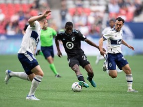 Minnesota United's DJ Taylor, centre, moves the ball past Vancouver Whitecaps' Russell Teibert, right, during the first half of an MLS soccer game in Vancouver, B.C., Friday, July 8, 2022.