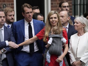 Carrie Johnson, the wife of Prime Minister Boris Johnson, touches the arm of Minister of State Nigel Adams, left, while listening to her husband read a statement outside 10 Downing Street, London, formally resigning as Conservative Party leader, in London, Thursday, July 7, 2022. Johnson said Thursday he will remain as British prime minister while a leadership contest is held to choose his successor.