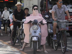 A woman covered up from the sun waits at a traffic junction, Wednesday, July 13, 2022, in Beijing.