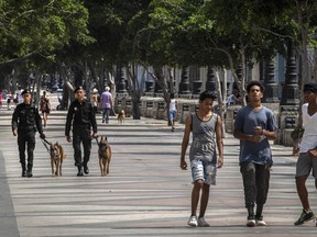 People walk at the Paseo del Prado while members of the police patrol in Havana, Cuba, Monday, July 11, 2022. A year after the largest protests in decades shook Cuba's single-party government, the economic and political factors that caused them largely remain.