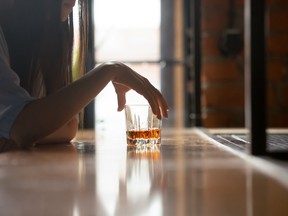 Sad young drinker alcoholic holding whiskey glass drinking alone sit at bar counter, upset stressed girl addicted to alcohol feel lonely frustrated suffer from alcoholism problem concept