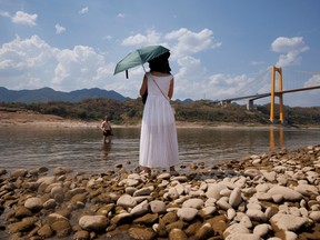 A woman watches her husband stand in the water from the dry riverbed of the Yangtze river that is approaching record-low water levels during a drought in Chongqing, China, August 20, 2022. REUTERS/Thomas Peter