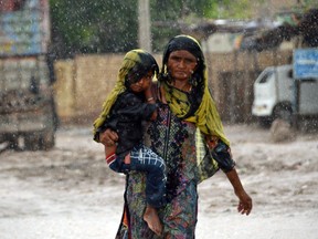 A woman carrying a child walks along a street during a heavy rainfall in the flood-hit Dera Allah Yar town in Jaffarabad district, Balochistan province, on August 30, 2022. - Aid efforts ramped up across flooded Pakistan on August 30 to help tens of millions of people affected by relentless monsoon rains that have submerged a third of the country and claimed more than 1,100 lives.