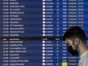 A person walks past a departures board full of delay notices at Toronto Pearson International Airport’s Terminal 1, July 7, 2022.