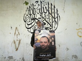 Palestinian Dalal Awawdeh poses with a poster of her husband Khalil Awawdeh, who is a prisoner in Israel, at the family house, in the West Bank village of Idna, Hebron, Tuesday, Aug. 9, 2022. Awawdeh, who is on a protracted hunger strike, was moved Thursday from an Israeli jail to a hospital because of his worsening condition, the prisoner's wife said. Arabic in the background reads "There is no God but Allah, Muhammad is the Messenger of Allah."