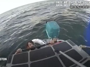 In this image taken from Boston Police Department video, the department's harbor patrol unit rescues a father and son clinging to a cooler after their boat sank in Boston Harbor on Wednesday, Aug. 24, 2022. (Boston Police Department via AP)