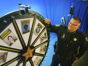 In this July 2017 photo, Brevard County Sheriff Wayne Ivey gets ready to spin his popular "Wheel of Fugitive" in Titusville, Fla. The popular videos feature photos of 10 of the county's most wanted criminals.