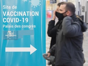People walk by a COVID-19 vaccination sign at a vaccination site in Montreal on Jan. 8, 2022. Quebec health officials say they are expecting to offer the new COVID-19 bivalent vaccine in less than two weeks.