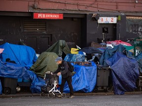 A man using a rolling walker walks on the street past tents setup on the sidewalk at a sprawling homeless encampment on East Hastings Street in the Downtown Eastside of Vancouver, on August 16, 2022. BC Housing says 40 people who were living in a Downtown Eastside street encampment being cleared by city workers have accepted offers of accommodation. The agency's vice-president of operations Dale McCann was speaking at a City Hall press conference today where Mayor Kennedy Stewart reported "good progress" clearing the street in accordance with a safety order by the city's fire chief.