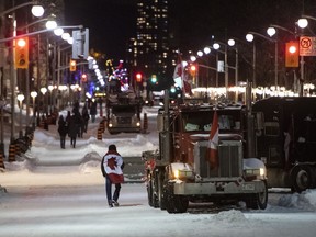 A person wearing a Canadian flag walks along Wellington Street where a number of trucks had cleared from an encampment across from Confederation Building, as police work to end an ongoing protest against COVID-19 measures that has grown into a broader anti-government protest in Ottawa on Friday, Feb. 18, 2022.