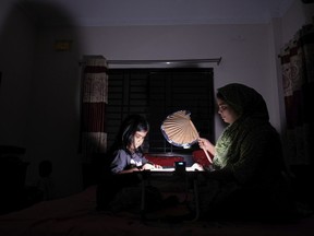 A Bangladeshi woman uses a traditional hand fan as she assists her daughter in her studies during a power cut at their home in Pilkhana area, Dhaka, Bangladesh, Tuesday, Aug.23, 2022. Schools in Bangladesh will close an additional day each week and government offices and banks will shorten their work days by an hour to reduce electricity usage amid concerns over rising fuel prices and the impact of the Ukraine war.