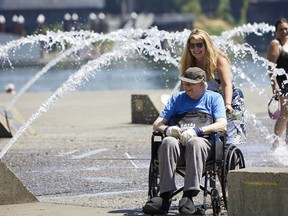 Stephanie Martin wheels her father Charles Calyear through the Salmon Street Springs fountain in Portland, Ore., Tuesday, July 26, 2022. Temperatures are expected to top 100 degrees F (37.8 C) on Tuesday and wide swaths of western Oregon and Washington are predicted to be well above historic averages throughout the week.