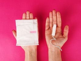 Woman holding menstrual tampon and pad on a pink background. Menstruation time. Hygiene and protection.