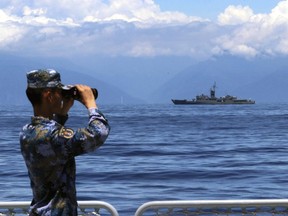 FILE - In this photo provided by China's Xinhua News Agency, a People's Liberation Army member looks through binoculars during military exercises as Taiwan's frigate Lan Yang is seen at the rear on Aug. 5, 2022. China on Wednesday, Aug. 10, reaffirmed its threat to use military force to bring self-governing Taiwan under its control, amid threatening Chinese military exercises that have raised tensions between the sides to their highest level in years.