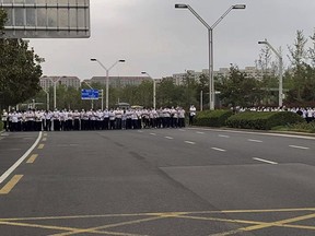 FILE - Plain clothes security personnel stand on the road as people protest at the entrance to a branch of China's central bank in Zhengzhou, Henan province on July 10, 2022. Provincial authorities announced on Monday, Aug. 29, 2022, the arrests of 234 people allegedly involved in a scam to bilk people out of their savings with the false promise of high interest rates. The scandal drew national attention after investors seeking information about their money were prevented from reaching Zhengzhou. (AP Photo/File)