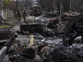 FILE - Soldiers walk amid destroyed Russian tanks in Bucha, in the outskirts of Kyiv, Ukraine, April 3, 2022. Six months ago, Russian President Vladimir Putin sent troops into Ukraine in an unprovoked act of aggression, starting the largest military conflict in Europe since World War II. Putin expected a quick victory but it has turned into a grinding war of attrition. Russian offensive are largely stuck as Ukrainian forces increasingly target key facilities far behind the front lines.