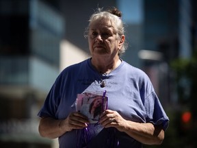 Deb Bailey holds a photograph of her late daughter, Ola "Izzy" Bailey, who died due to an illicit drug overdose in 2015, as members of Moms Stop the Harm hang photos of those who have died on trees and light posts in downtown Vancouver on Tuesday, Aug. 16, 2022.