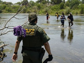 FILE - A Border Patrol agent watches as a group of migrants walk across the Rio Grande on their way to turn themselves in upon crossing the U.S.-Mexico border in Del Rio, Texas, on June 15, 2021. The Supreme Court has certified its month-old ruling allowing the Biden administration to end a cornerstone Trump-era border policy to make asylum-seekers wait in Mexico for hearings in U.S. immigration court. It was a pro forma act that has drawn attention amid near-total silence from the White House about when, how and even whether it will dismantle the policy.