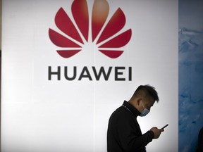 FILE - A man wearing a face mask walks past a billboard advertising Chinese technology firm Huawei at the PT Expo in Beijing, Oct. 14, 2020. Chinese tech giant Huawei said Friday, Aug. 12, 2022 its revenue fell in the first half of 2022 but new ventures in autos and other industries helped to offset a decline in smartphone sales under U.S. sanctions.
