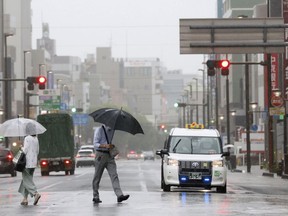 People walk in the rain in front of a station, Saturday, Aug. 13, 2022, in Shizuoka, west of Tokyo. Tropical Storm Meari is unleashing heavy rains on southwestern Japan as it heads northward toward the Tokyo capital, according to Japanese weather officials.