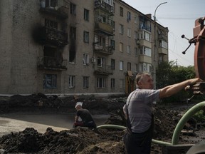 Workers drain water from a crater created by an explosion that damaged a residential building after a Russian attack in Slovyansk, Ukraine, Sunday, Aug. 28, 2022.