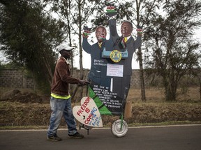 A supporter of Kenya's President-elect William Ruto pushes a cart with cardboard cutout of the president and his running mate, outside the official residence of the deputy president in the Karen area of Nairobi, Kenya Wednesday, Aug. 17, 2022.