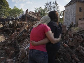 Ukrainian women hug in front of a building destroyed during a missile strike in Kharkiv, Ukraine, Thursday, Aug. 18, 2022.