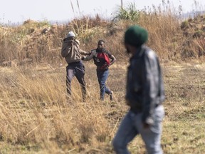 CORRECTS AS IMAGE DOES NOT SHOW PEOPLE RUNNING FROM TEAR GAS AND STUNT GRENADES - A resident, left, grabs a man suspected of being an illegal miner in the South African city of Krugersdorp Thursday Aug. 4, 2022. Community members in the assaulted suspected illegal miners and set fire to their camps on Thursday in an outpouring of anger following the alleged gang rapes of eight women by miners last week. Residents of Krugersdorp's Kagiso township also barricaded roads with rocks and burning tires during a planned protest.