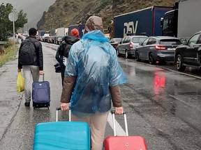 People carrying luggage walk past vehicles with Russian license plates on the Russian side of the border towards the Nizhniy Lars customs checkpoint between Georgia and Russia some 25 km outside the town of Vladikavkaz, on September 25, 2022.