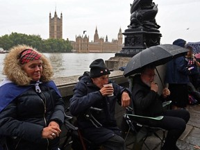 Members of the public queue in the rain along the south bank of the River Thames, opposite the Palace of Westminster, home to Westminster Hall and the Houses of Parliament, in London on September 13, 2022, as they wait to pay their respects when Queen Elizabeth II Lies in State.