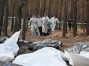 Forensics carry body bags in a forest near Izyum, Ukraine, on Sept. 19, where Ukrainian investigators have uncovered more than 440 graves after the city was recaptured from the Russians, bringing fresh claims of Russian atrocities.