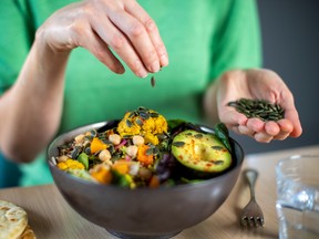 Close Up Of Woman Adding Pumpkin Seeds To Healthy Vegan Meal In Bowl