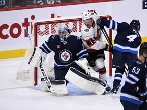 Winnipeg Jets' Neal Pionk (4) and Ottawa Senators' Jayce Hawryluk (13) battle for position as goaltender Connor Hellebuyck (37) watches the shot rebound during the second period of NHL pre-season action in Winnipeg on Tuesday September 27, 2022.