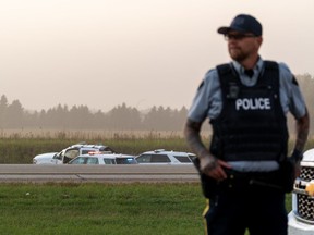 Police and investigators are seen at the side of the road outside Rosthern, Sask., on Wednesday, Sept. 7, 2022. Myles Sanderson, a suspect in a deadly series of stabbings in Saskatchewan, was caught by police on a highway, arrested, and died, RCMP said Wednesday.