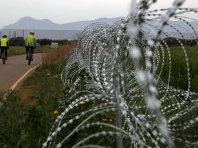 FILE - Two men cycle along a row of razor wire along the southern side of a U.N buffer zone that cuts across the ethnically divided Cyprus, during sunset near village of Astromeritis, on March 9, 2021. Cyprus is seeking help from the United Nations to stem an "avalanche" of migrants who make their way from the ethnically divided island's breakaway north across a UN controlled buffer zone to seek asylum in numbers that authorities cannot cope with, the Cypriot interior minister said Monday Sept. 26, 2022.