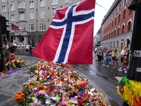 FILE - A Norwegian national flag flutters over flowers and rainbow flags that are placed at the scene of a shooting in central of Oslo, Norway, on June 26, 2022. A Norwegian citizen in his 40s is being sought after for his role in the deadly shooting in June in Oslo's nightlife district during the capital's annual LGBTQ Pride festival, police said Friday Sept. 23, 2022. Another suspect has already been arrested.