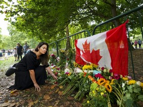 Canadian Kersten Samolczyk who now resides in the United Kingdom places flowers by a Canadian flag as thousands of mourners lay flowers as people pay their respects near the gates of Buckingham Palace in London on Sunday, September 11, 2022.